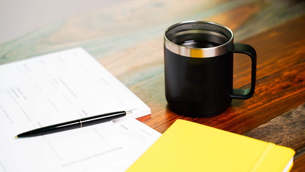 An image of coffee beside various papers and a pen on top of a desk.